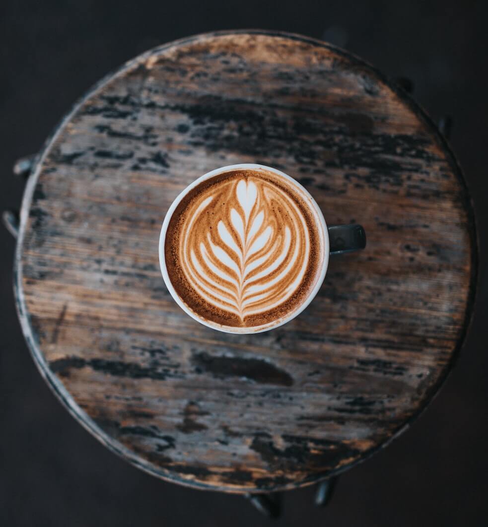 Flat White in einer Tasse auf einem runden Holztisch